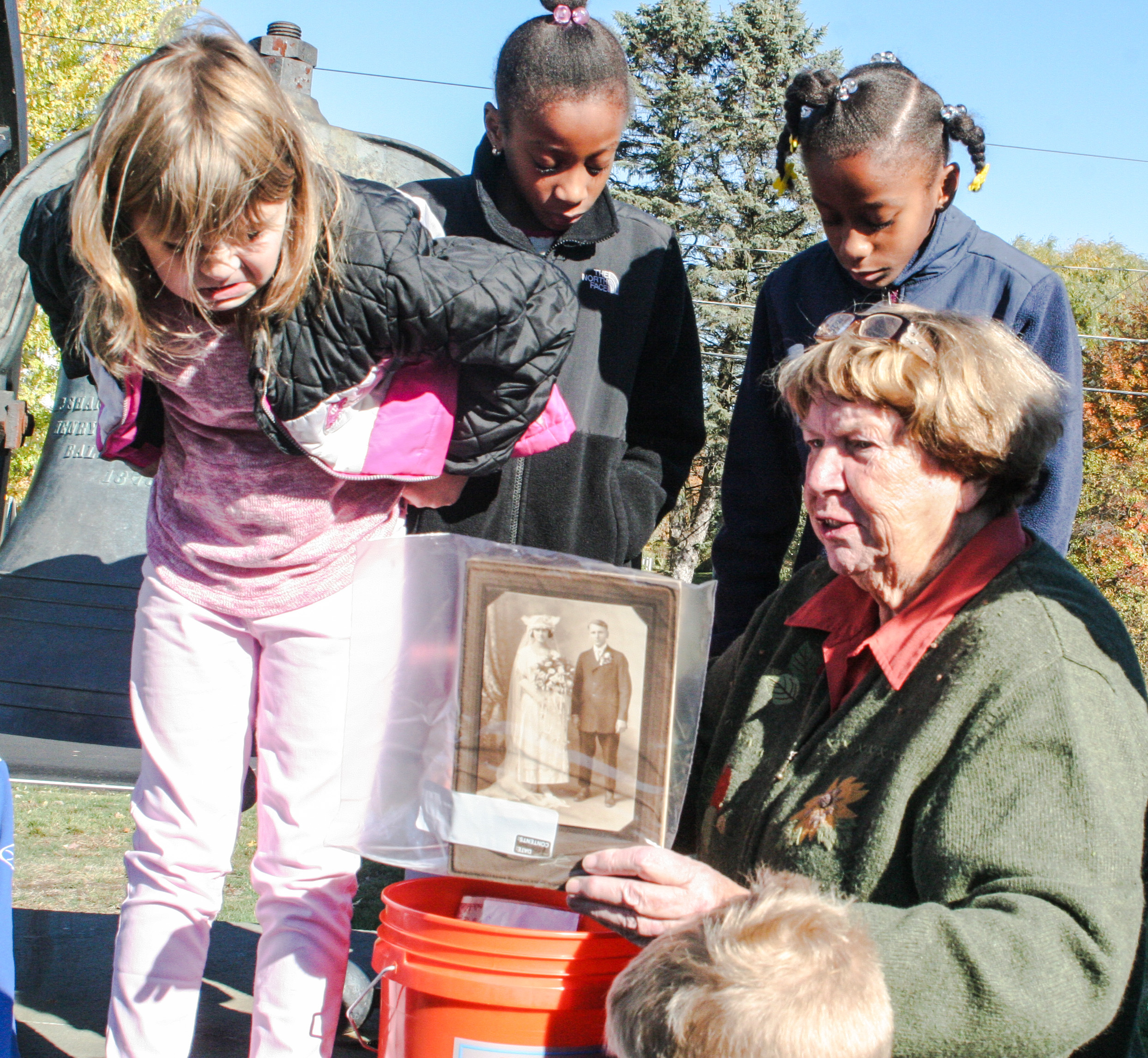 Chairperson Carol Griffin explaining time capsule with children looking on